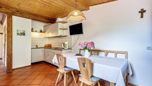 A kitchen with wooden ceiling, white walls, a TV mounted above the counter, and a dining table set with chairs. - Mayrhof Ahorn Apartment with Mountain View, Wi-Fi & Balcony (St. Pankraz)