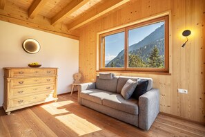 Un intérieur en bois comprenant un canapé, une commode en bois, une fenêtre donnant sur la montagne et un luminaire fixé au mur.