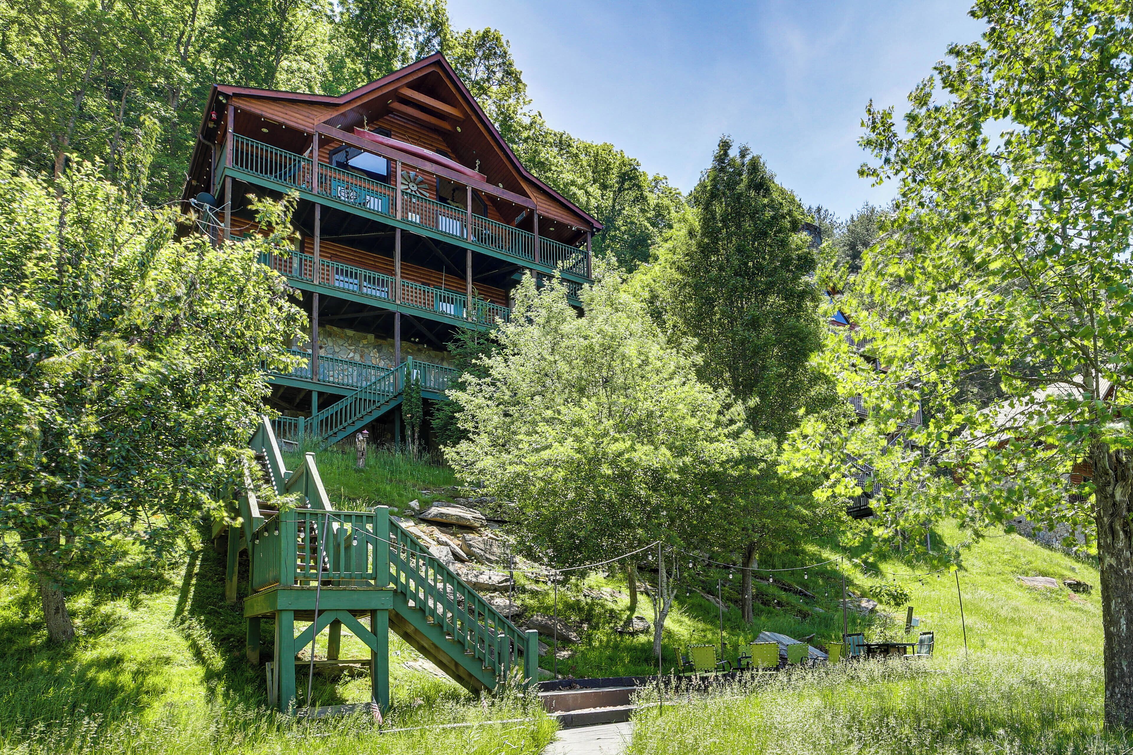 A multi-story log cabin with a balcony, surrounded by lush greenery and a stone staircase.