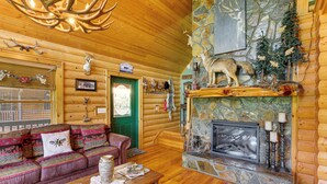 A log cabin interior with a stone fireplace, a green door, a wooden ceiling, and a plush red sofa. - 'River Dream Cabin' on New River w/ Fire Pit (Piney Creek)