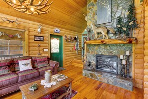A log cabin interior with a stone fireplace, a green door, a wooden ceiling, and a plush red sofa.