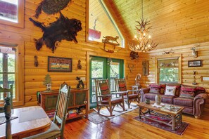 A log cabin interior with a wooden floor, a sofa, rocking chairs, a coffee table, and a chandelier.