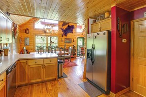 A cabin interior with wooden floors, a kitchen with a refrigerator, wooden cabinets, and a dining area with chairs and a table.