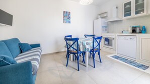 A compact living space with a sofa, dining table, chairs, and a kitchen area including a dishwasher and oven. - Appartamento Playa Iside - Torre... (Torre lapillo)