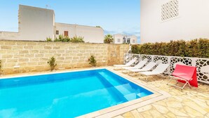 A swimming pool with lounge chairs, a stone wall, and a white building with a geometric pattern. - Appartamento Playa Lapillo - Tor... (Boncore)