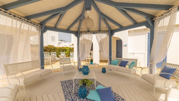A covered outdoor seating area with white furniture and blue cushions, a patterned rug, and a hanging light fixture. - Appartamento Playa Lapillo - Tor... (Boncore)