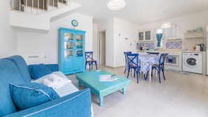 A modern living room with a blue sofa, a matching ottoman, and a dining area with blue chairs and a table. - Appartamento Playa Lapillo - Tor... (Boncore)