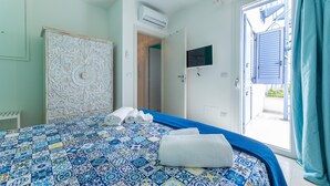 A bedroom with a patterned bedspread, a wardrobe, a flat-screen TV, and a view of the outside. - Appartamento Playa Lapillo - Tor... (Boncore)