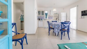 A modern kitchen with white cabinets, a dining area with blue chairs, and a teal-colored table. - Appartamento Playa Lapillo - Tor... (Boncore)