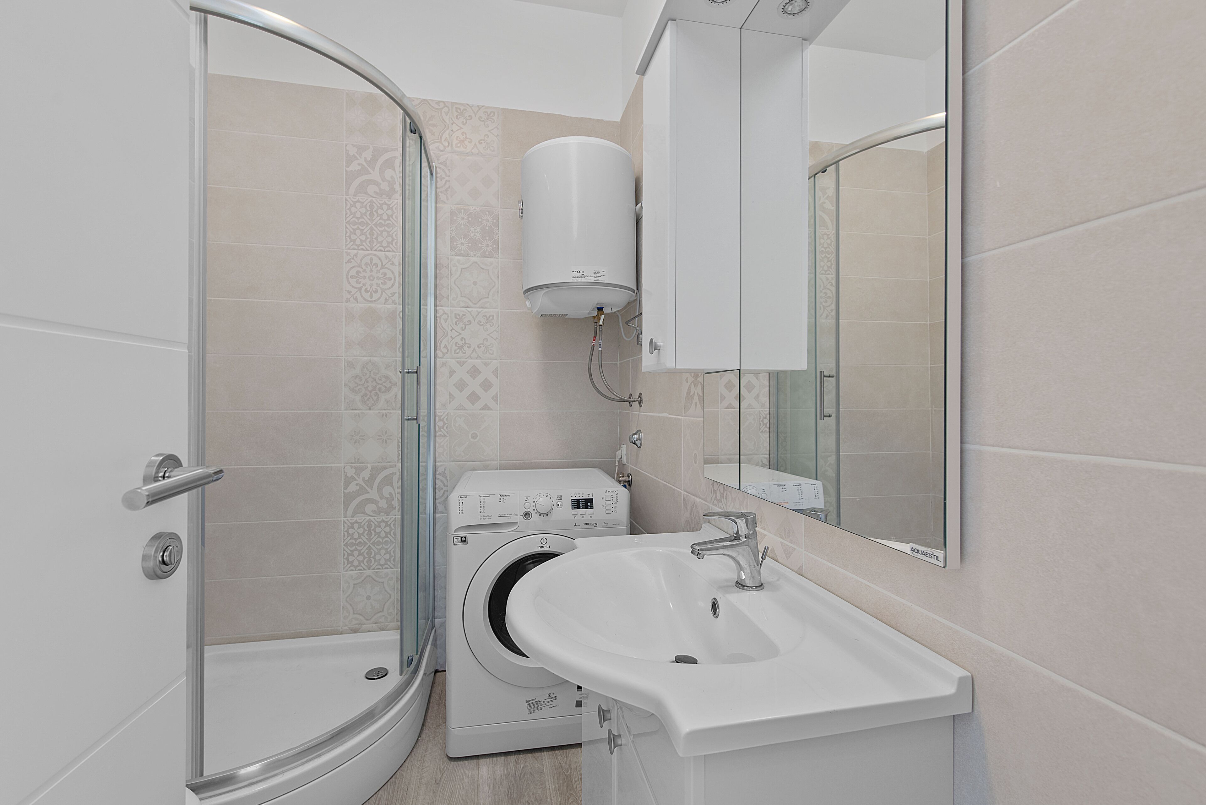 Un bagno moderno con box doccia in vetro, lavatrice a incasso e lavandino con specchio sopra.