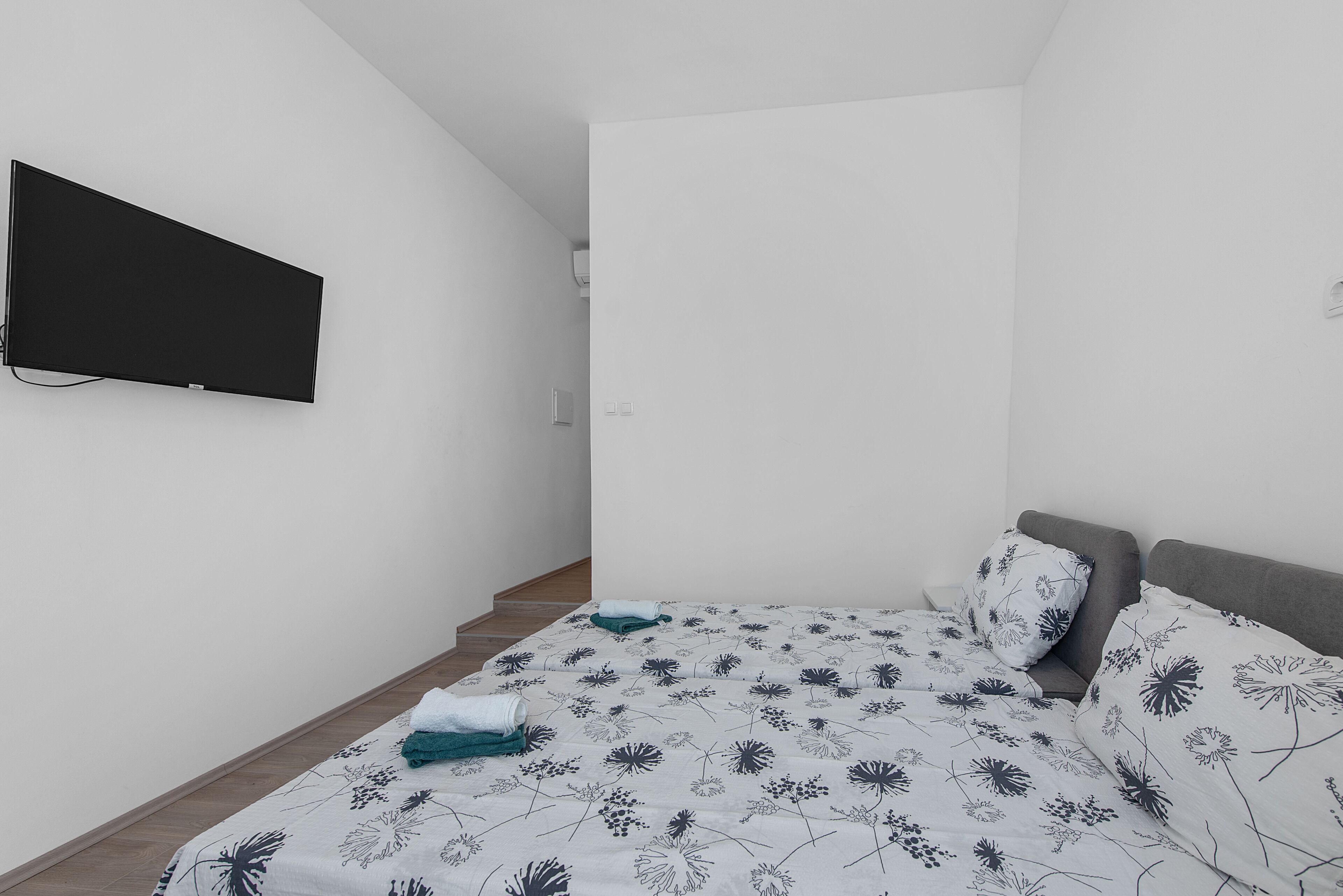 A bedroom with a bed, a flat-screen TV mounted on the wall, and a staircase leading to another room.