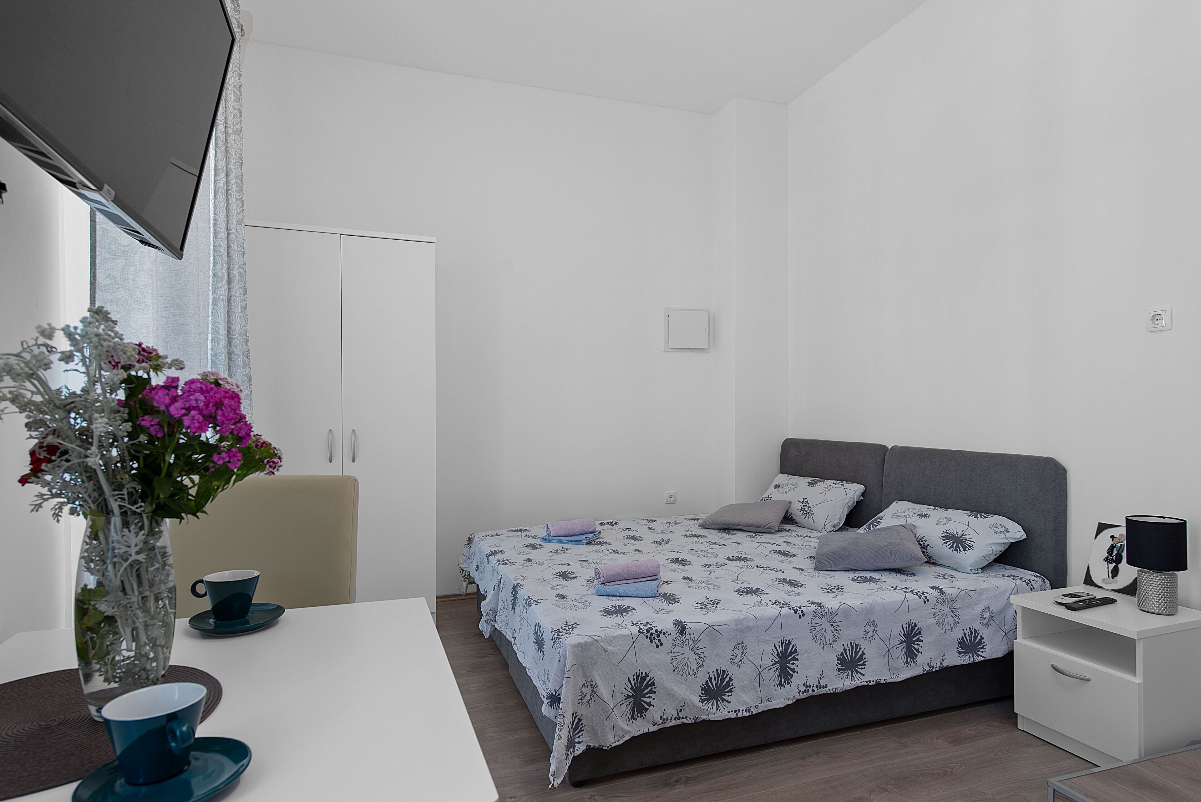 Une chambre à coucher moderne avec un lit, une table de chevet et un vase rempli de fleurs.