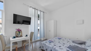 A bedroom with a bed, a desk with a chair, a TV, and a wardrobe.