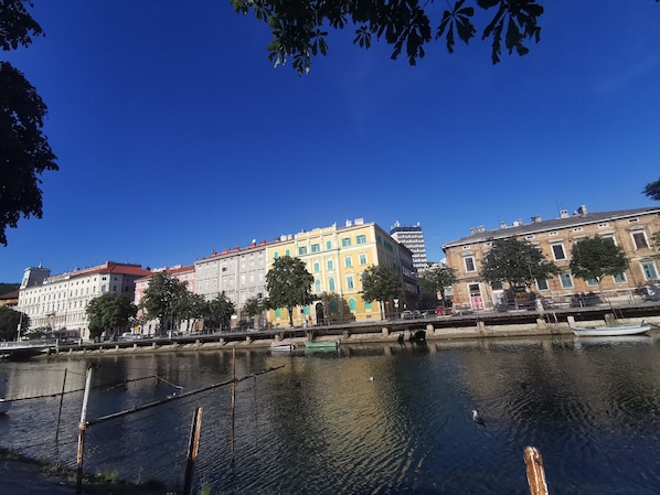 Un río con edificios a lo largo de su orilla, incluyendo un hotel con techo rojo y un edificio moderno con un letrero azul.