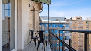 A balcony with two chairs and a table, overlooking a cityscape with buildings of various heights and colors.