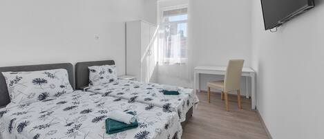 A bedroom with two beds, a desk, a chair, and a TV.