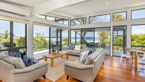 A spacious living area with large windows offering ocean views, a wooden coffee table, and comfortable seating. - Aiyana.. coastal indulgence at Blueys Beach! (Blueys Beach)