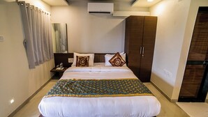 A neatly made bed with a patterned bedspread, a nightstand with a lamp, and a wardrobe in a hotel room. - Saanvi Resort Bhavnagar (Bhavnagar)