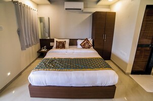 A neatly made bed with a patterned bedspread, a nightstand with a lamp, and a wardrobe in a hotel room.