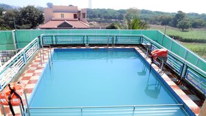 A rectangular swimming pool with a blue water surface, surrounded by a green fence and a white railing. - Saanvi Resort Bhavnagar (Bhavnagar)