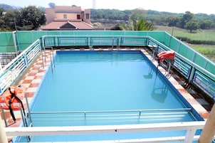 A rectangular swimming pool with a blue water surface, surrounded by a green fence and a white railing.