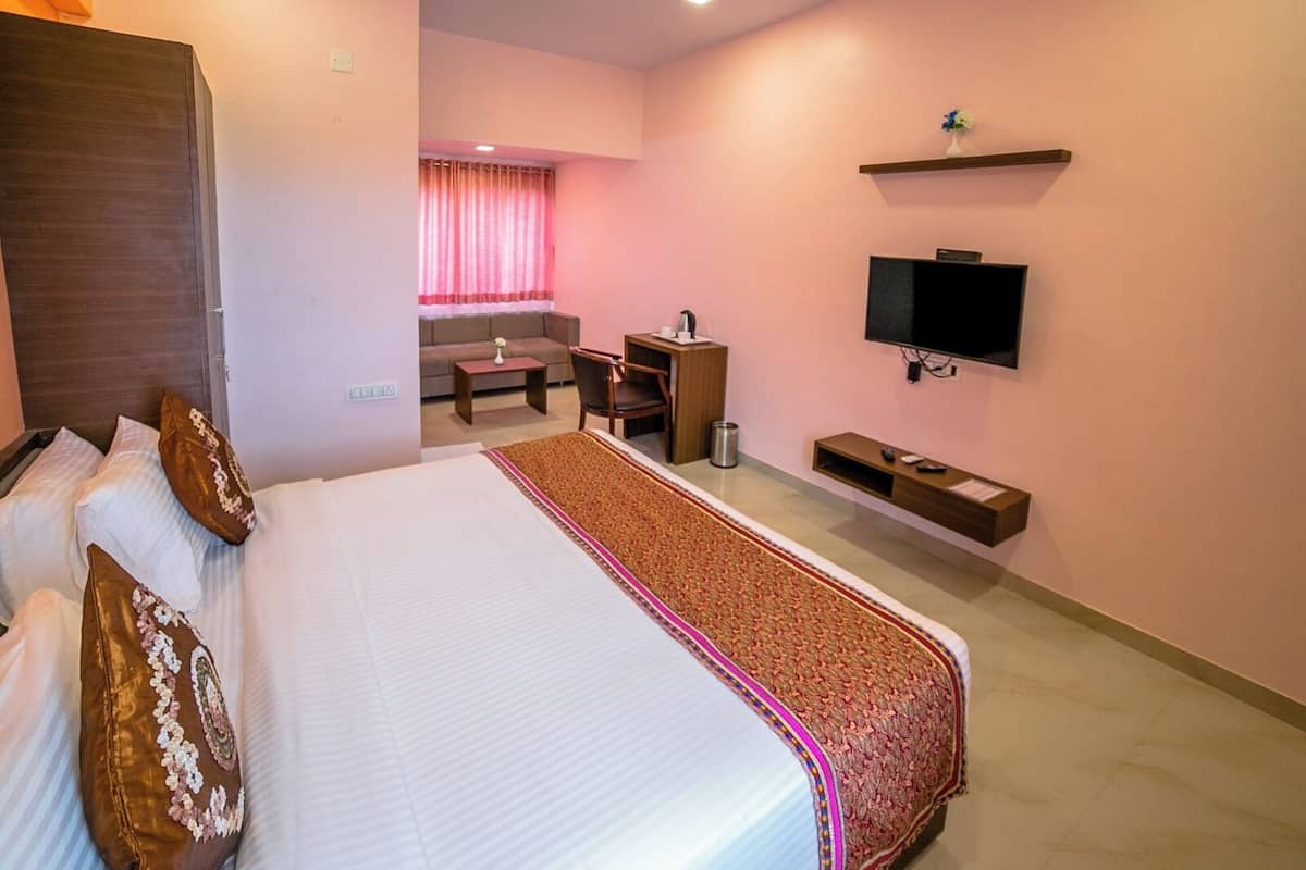 Quarto de hotel com cama grande, televisão na parede, escrivaninha com cadeira e pequena área de kitchenette.