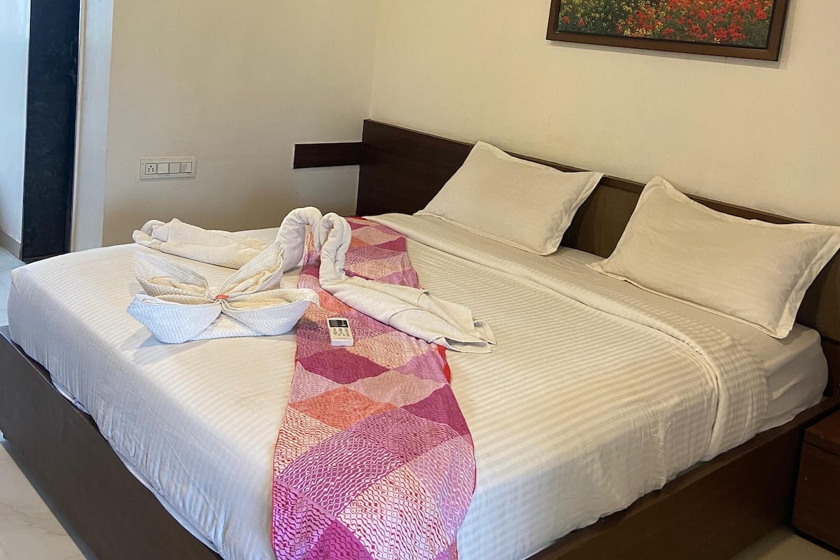 Uma cama bem arrumada com um cobertor estampado, um ventilador de teto, ar condicionado e um quadro com uma paisagem na parede.