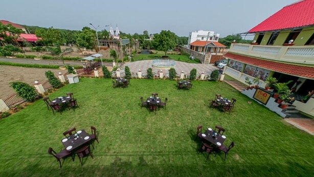 A courtyard with multiple tables and chairs, surrounded by buildings and greenery. - Saanvi Resort Bhavnagar (Bhavnagar)