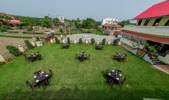 A courtyard with multiple tables and chairs, surrounded by buildings and greenery.