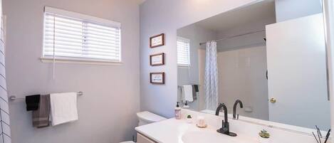 A bathroom with a white sink, a large mirror, and a toilet. There are three framed pictures on the wall and a towel rack with towels.