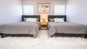 A bedroom with two beds, a white fluffy rug, a framed picture on the wall, and a nightstand with lamps.