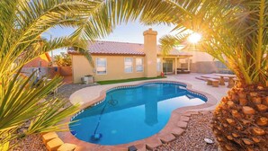 A swimming pool with a curved edge, surrounded by a pebble border and palm trees.