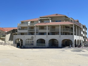 Ein mehrstöckiges Hotel mit Balkonen, einem überdachten Eingang und sandigem Untergrund.