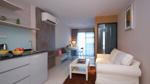Un salon moderne avec un canapé blanc, une table basse et un coin cuisine équipé d’un évier et d’un panier de fruits.