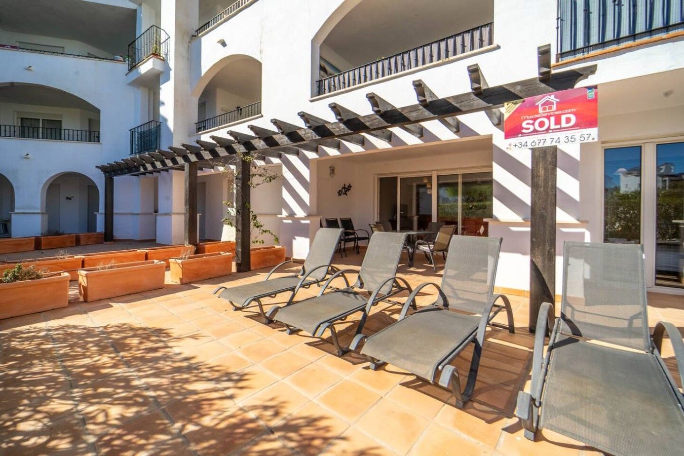 A property with a pergola, outdoor seating, and a 'SOLD' sign.
