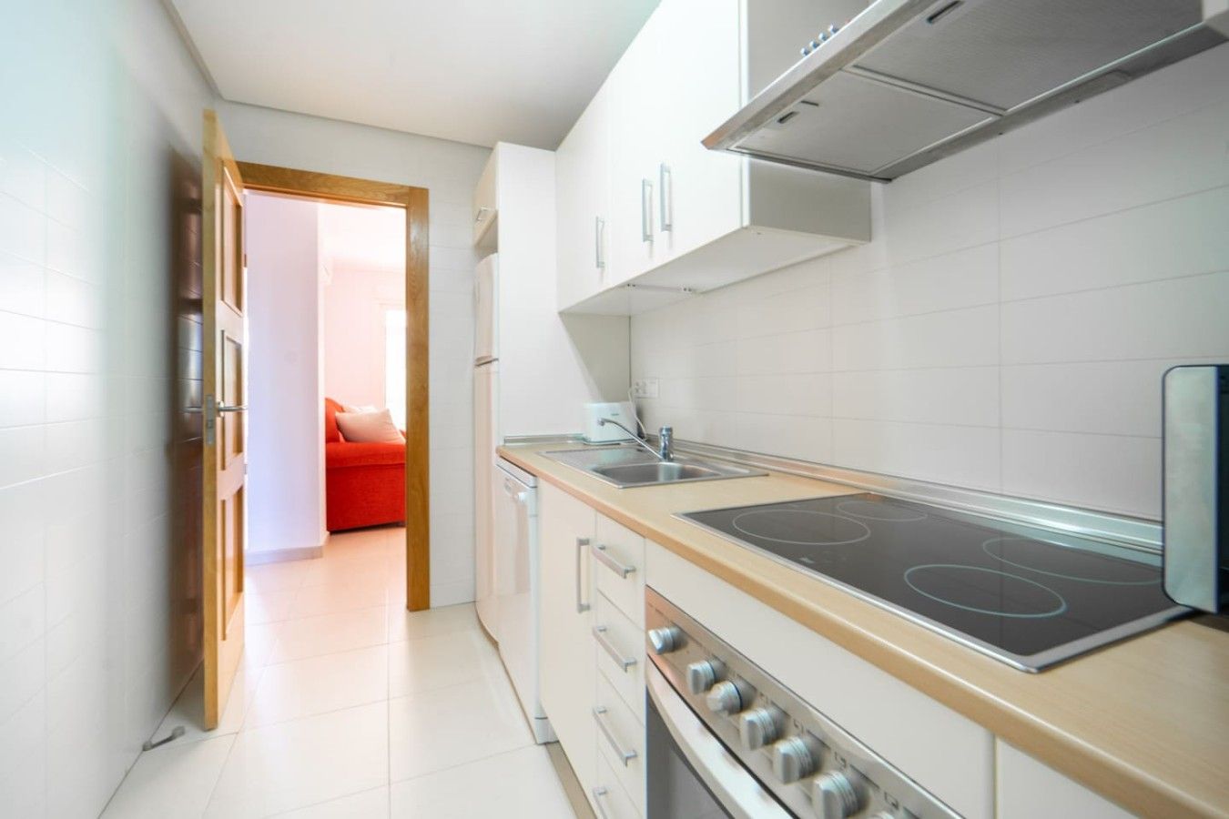 A modern kitchen with white cabinets, a stainless steel range hood, and a built-in stovetop.