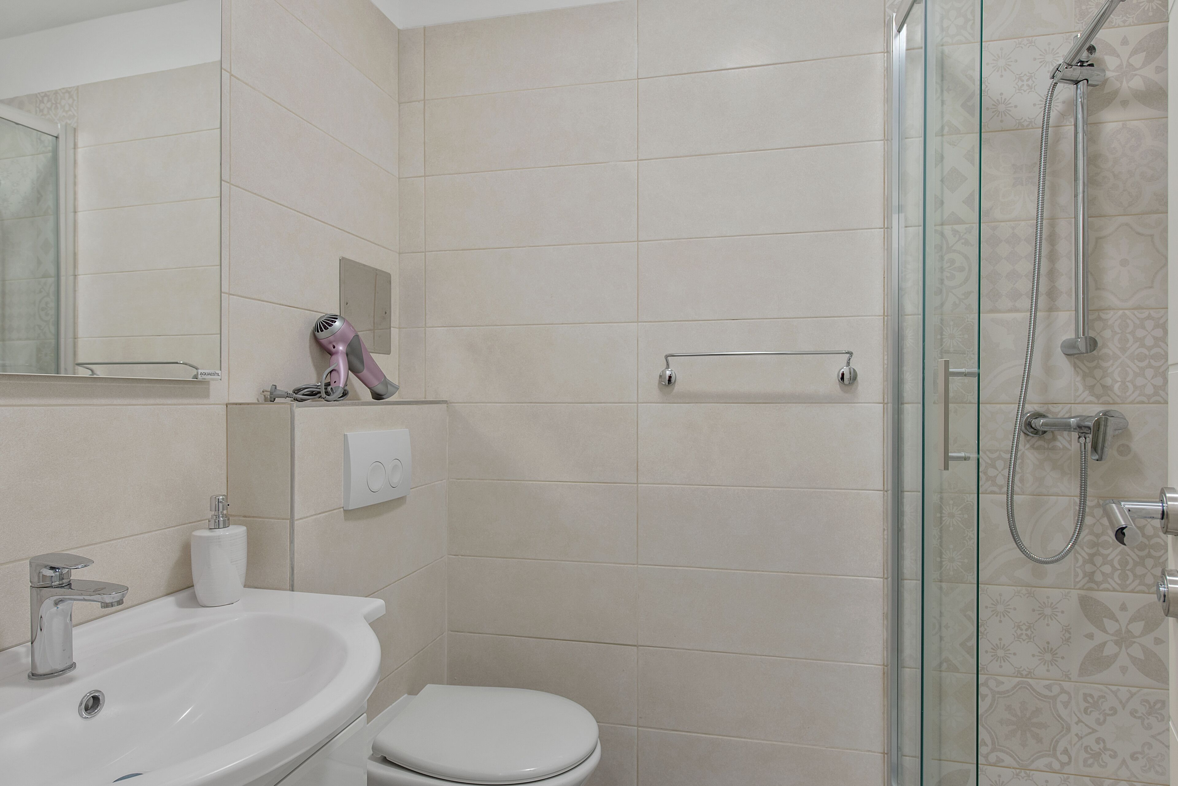 Une salle de bain équipée d’un lavabo, de toilettes et d’une douche séparée par des parois en verre.