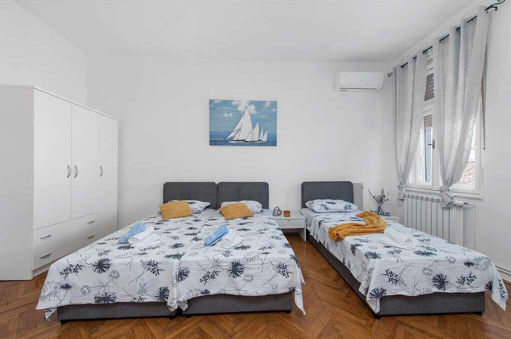 Un dormitori amb dos llits, un armari blanc, un quadre de velers i una finestra amb cortines.