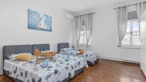 A room with two beds, a dining table with breakfast, and a painting of sailboats. - La Guardia apartments (Rijeka)