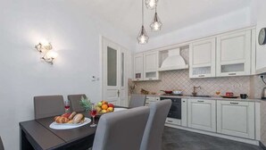 A modern kitchen with white cabinets, a dining table with chairs, and a fruit bowl on the table. - La Guardia apartments (Rijeka)
