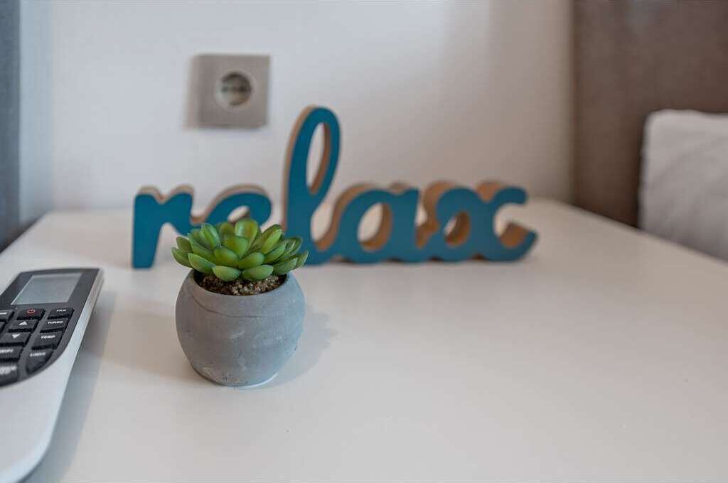 Une petite plante en pot est posée sur une surface blanche, à côté d’un clavier et d’un mur sur lequel est écrit le mot « relax » en lettres bleues.