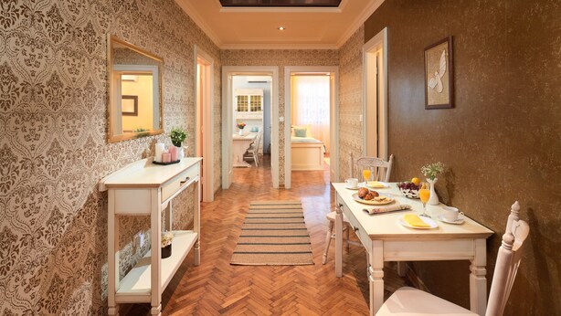 Habitació d'hotel amb sòl de fusta en relleu de serra, zona de dinar amb taula preparada per esmorzar i un mirall a la paret esquerra.