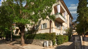 Un edifici residencial de diversos pisos amb balcons, envoltat d'arbres i una paret de pedra.