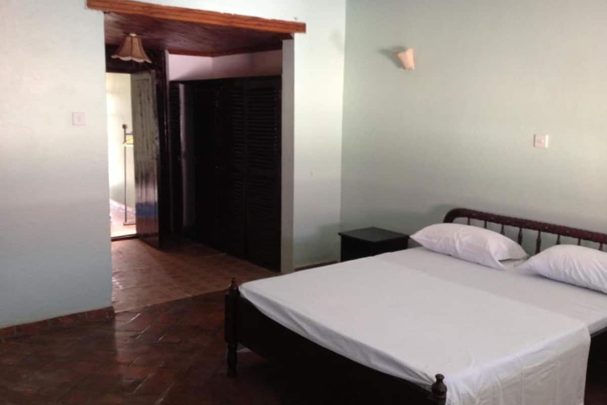A bedroom with a bed, a nightstand, and a door leading to another room.