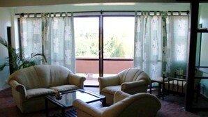 Una sala de estar con dos sillones, una mesa de centro y vista a un balcón exterior a través de una puerta de vidrio.