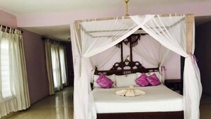 Una cama con dosel, ropa de cama blanca y almohadas moradas.