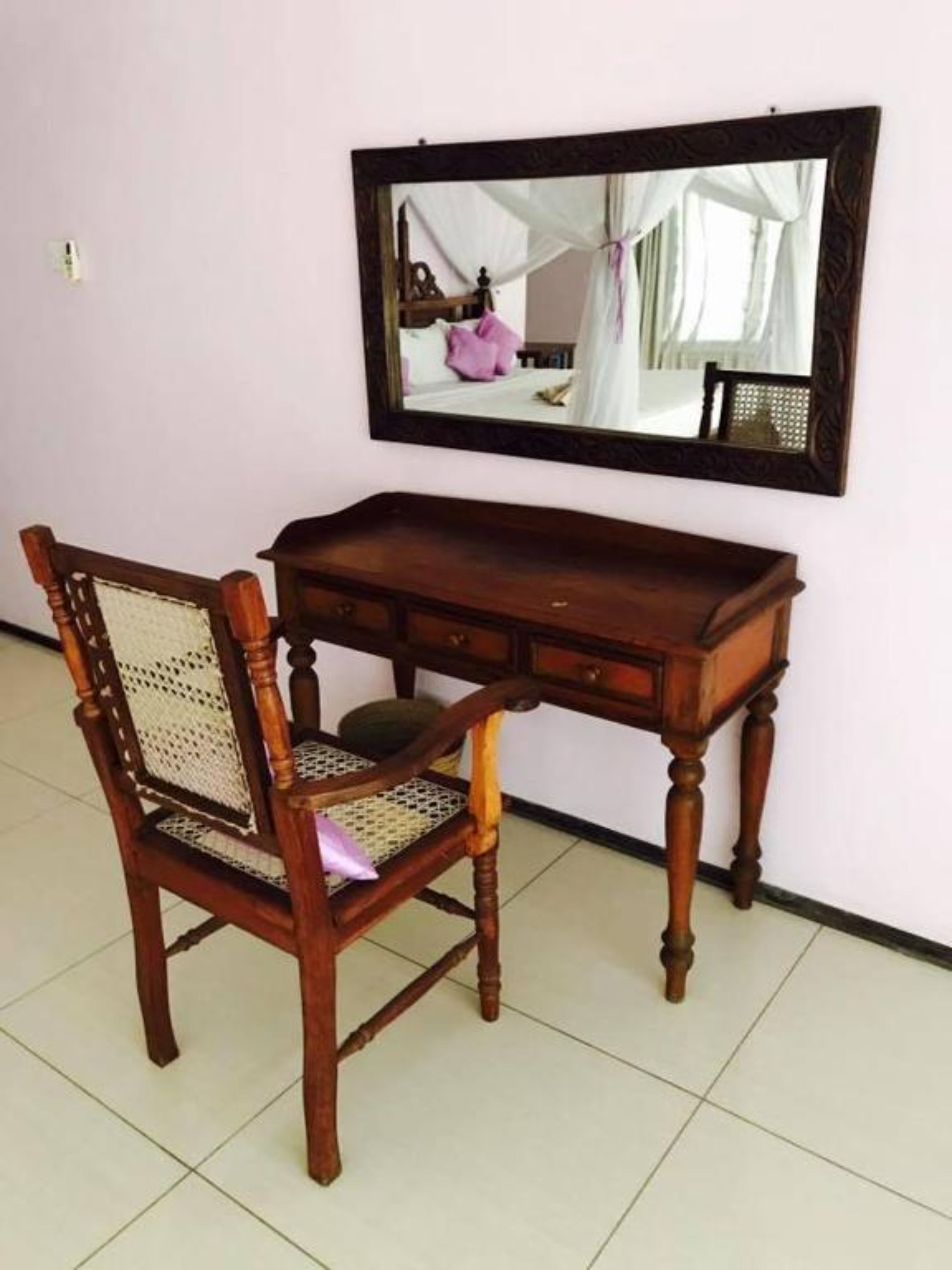 Un bureau en bois avec un miroir au-dessus, une chaise en osier et un sol carrelé.