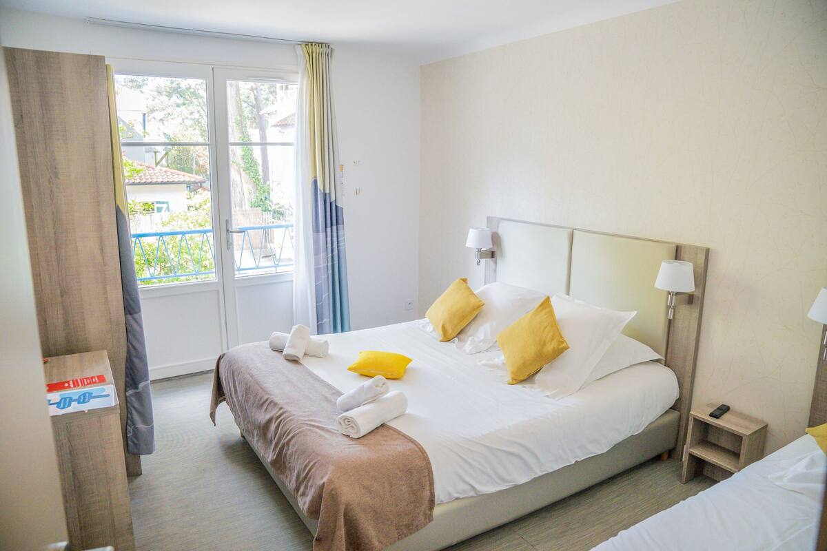 A hotel room with a bed, a nightstand, a lamp, and a view of the outside.