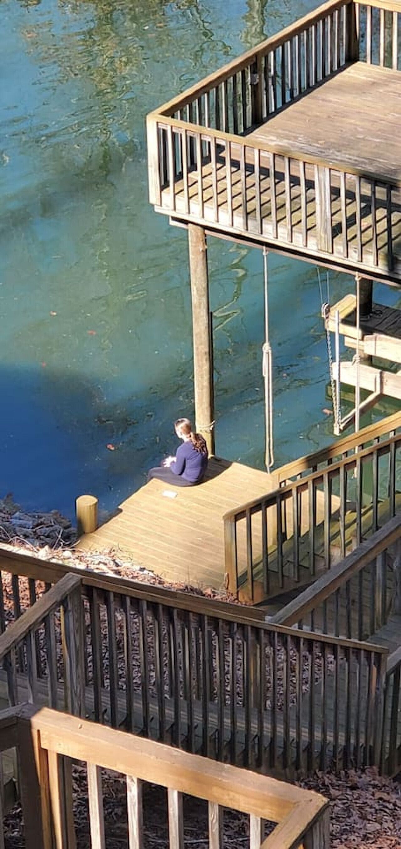 A wooden deck with a person sitting on it, overlooking a body of water.
