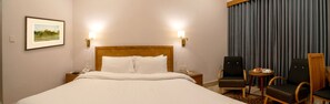 A hotel room with a large bed, two bedside tables, a chair, a small table with a plate and a glass, and a framed picture on the wall.